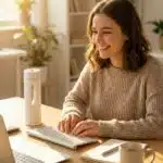 Weiße Hydrogen-Wasserflasche auf einem Holzschreibtisch neben einer lächelnden Frau im Homeoffice.